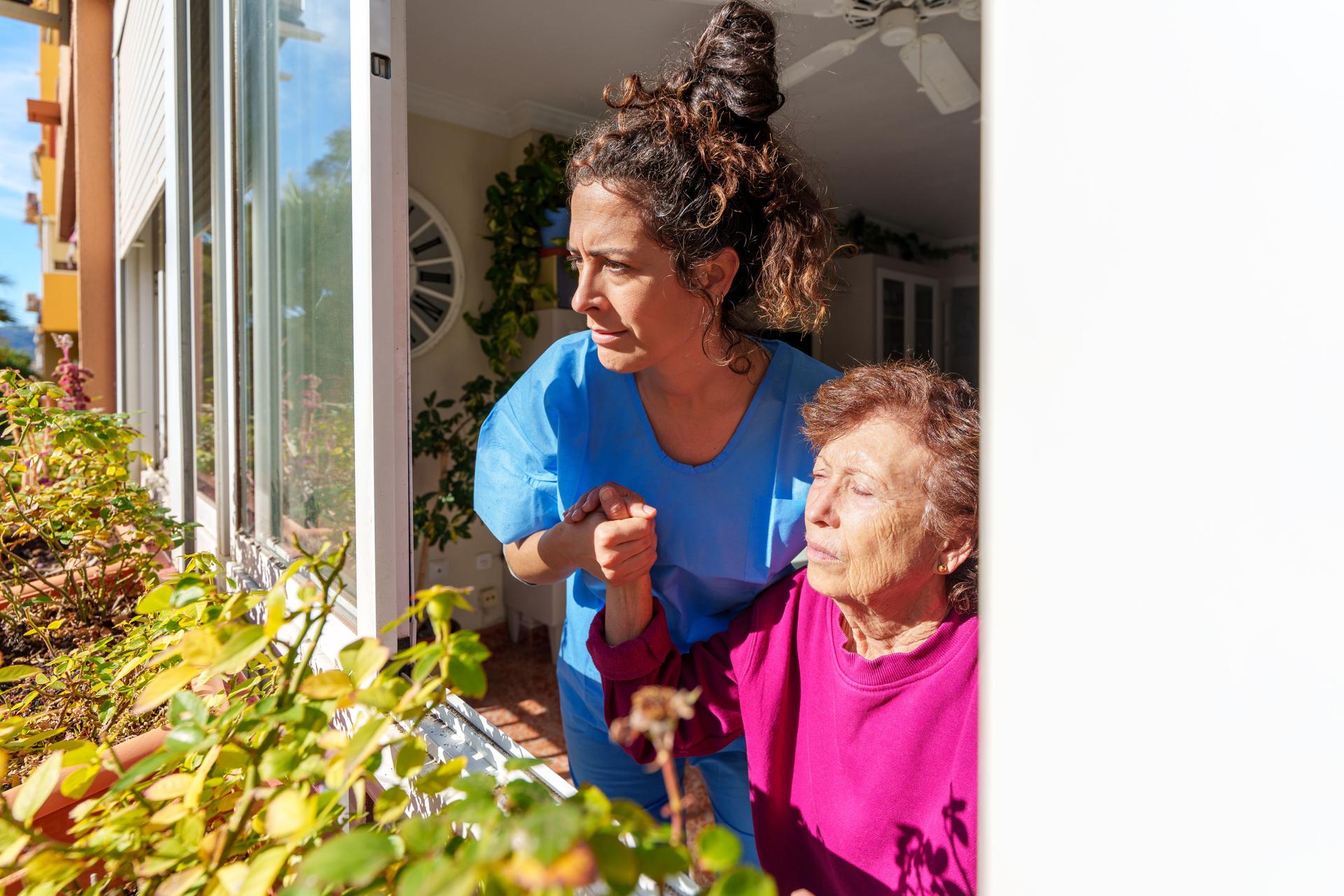 Caregiver accompanying elderly woman checking plants on balcony